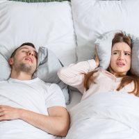 Man snoring in bed, woman covering her ears with a pillow | Intus Healthcare